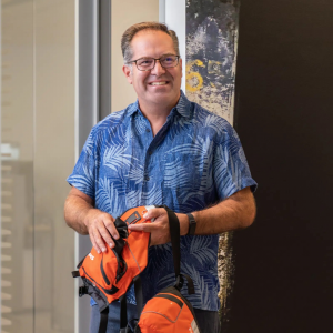 Photo of William M. Bruin in a Hawaiian shirt and holding two neon orange fanny packs.
